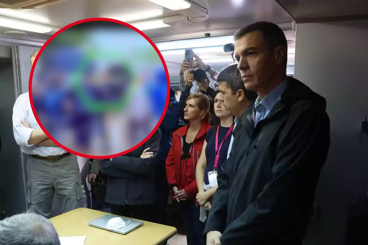 Un grupo de personas de pie en una sala, algunas con chaquetas, observando atentamente algo fuera de la imagen.