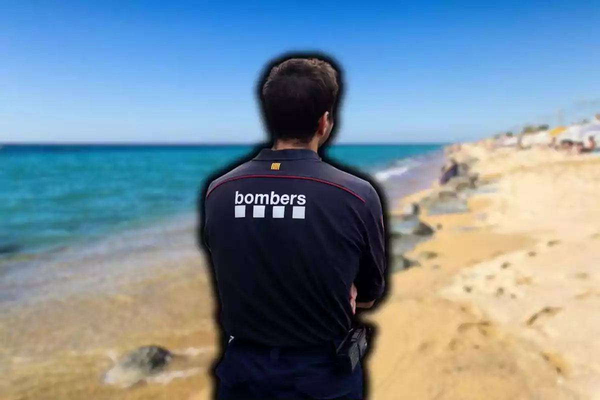 Un bomber dʻesquena a la platja amb el mar de fons.