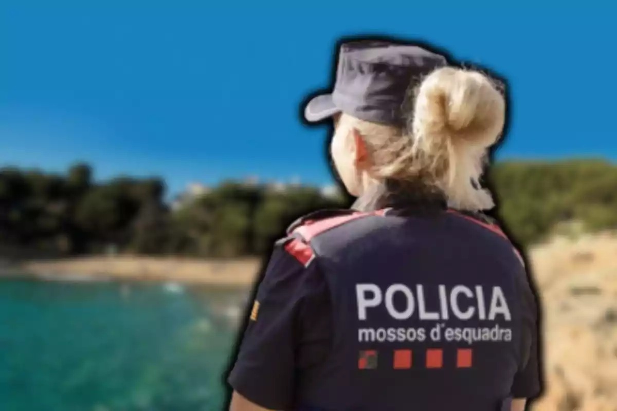 Agent de la policia dels Mossos d'Esquadra d'esquena amb uniforme, observant un paisatge costaner amb cel clar.