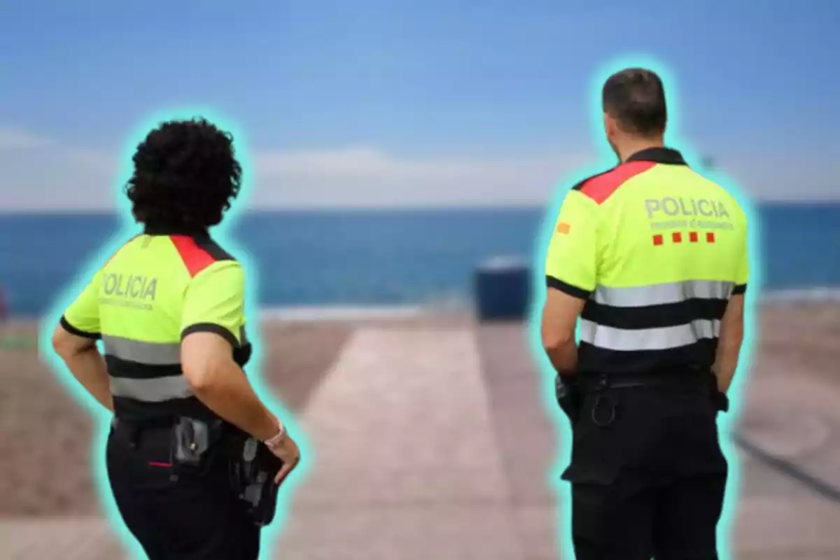 Dos policies d'esquena mirant cap al mar a una platja.