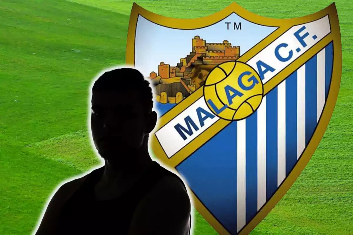 Una silueta oscura frente al escudo del Málaga C.F. sobre un campo de fútbol verde.