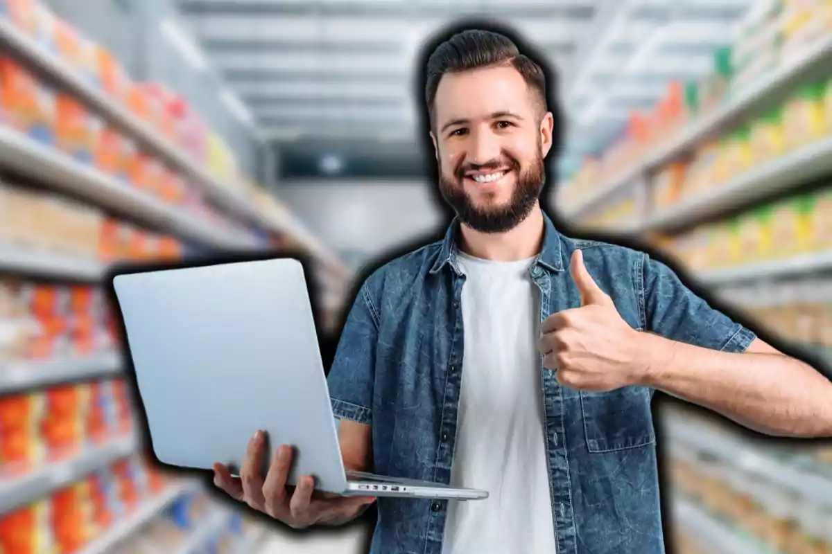 Hombre sonriente con barba sosteniendo una laptop y haciendo un gesto de aprobación con el pulgar en un pasillo de supermercado.