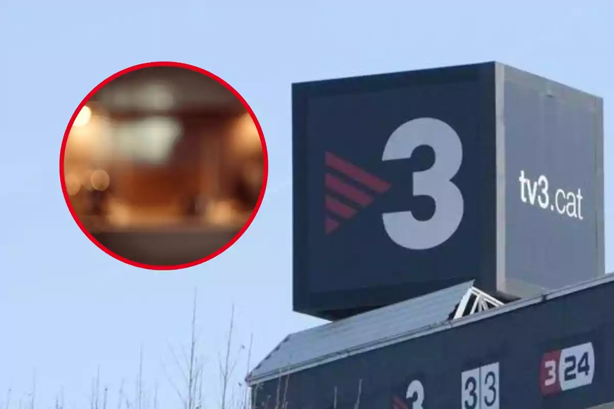 Un cartell gran de TV3 amb el logo i l'adreça web en un edifici sota un cel blau.