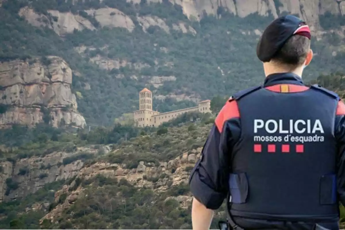 Un agente de los Mossos d'Esquadra observa un paisaje montañoso con un edificio histórico al fondo.