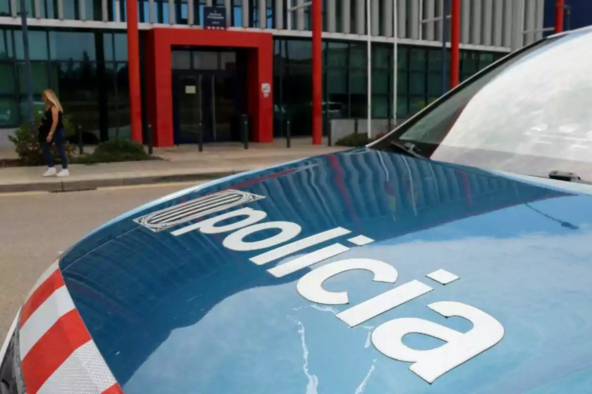 Un cotxe de policia estacionat davant d'un edifici amb una persona caminant a prop.