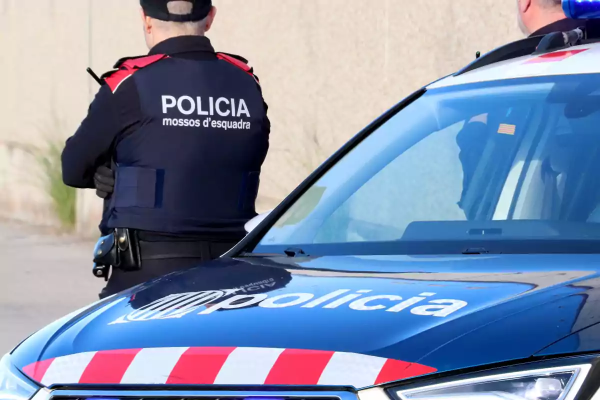 Un agent de policia d'esquena al costat d'un cotxe patrulla dels Mossos d'Esquadra.