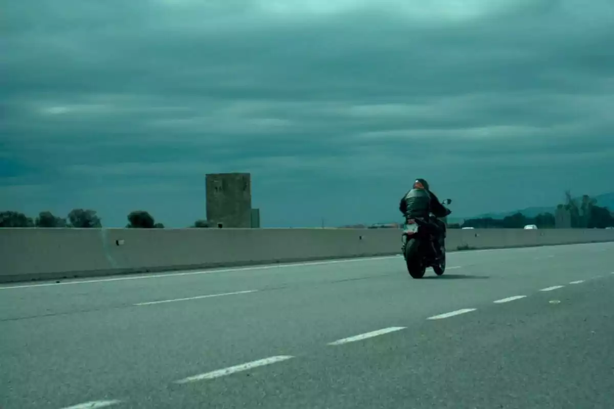 Motociclista conduciendo en una carretera vacía bajo un cielo nublado.