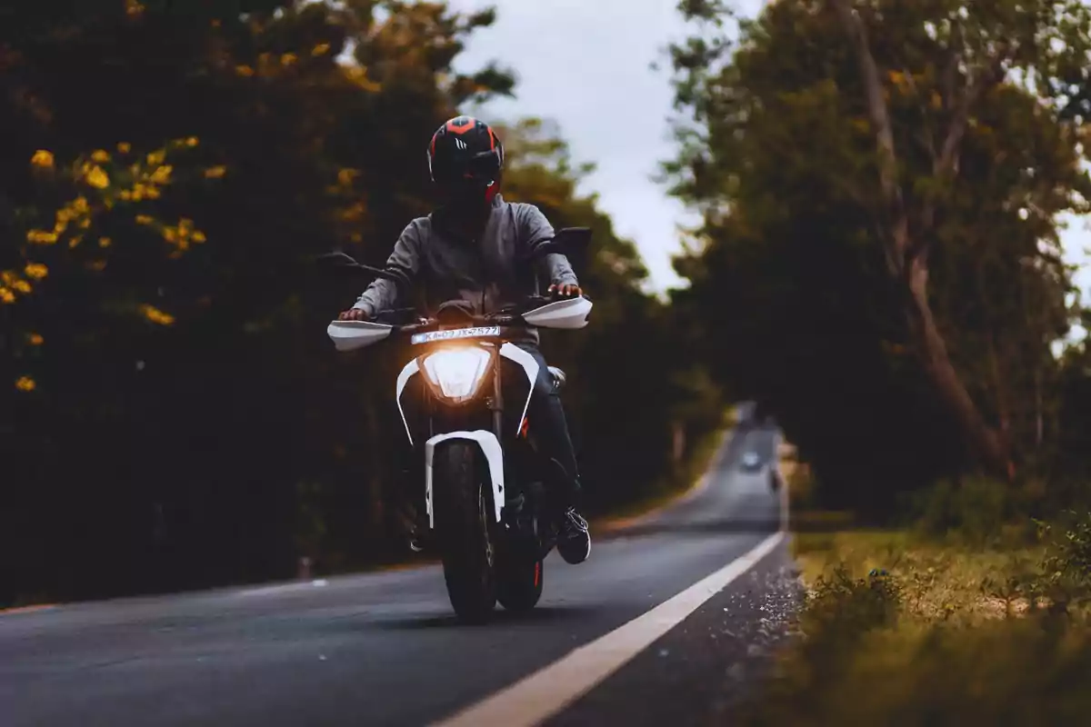 Motociclista amb casc negre i vermell conduint una motocicleta a una carretera envoltada d'arbres. Motociclista amb casc negre i vermell conduint una motocicleta a una carretera envoltada d'arbres.