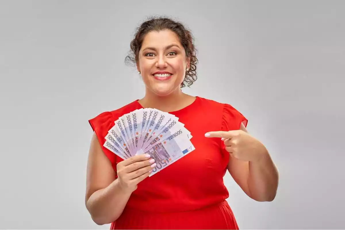 Una dona somrient mentre assenyala un feix de bitllets de 500 euros que té a la mà dreta