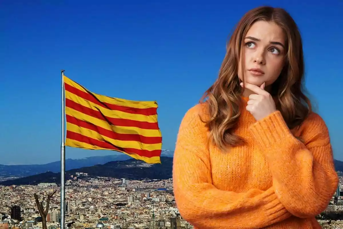 Dona pensativa amb un suèter taronja davant d'una bandera catalana onejant sobre una ciutat.