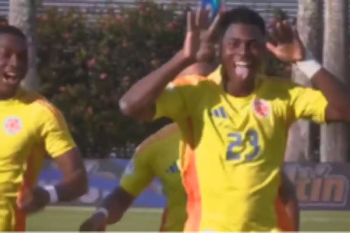 Un grupo de jugadores de fútbol con uniformes amarillos celebrando en el campo, uno de ellos hace un gesto divertido con las manos y saca la lengua. Un grupo de jugadores de fútbol con uniformes amarillos celebrando en el campo, uno de ellos hace un gesto divertido con las manos y saca la lengua.