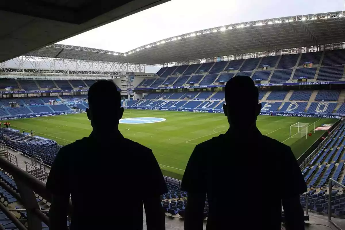 Muntatge amb una imatge del Carlos Tartiere, estadi del Real Oviedo, de fons. En primer terme dues ombres negres dhome