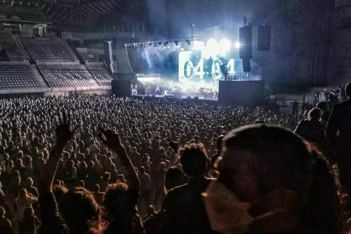 Una multitud gaudeix d´un concert en un estadi amb llums brillants i un gran escenari al fons.