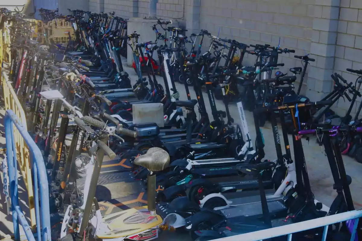 Una gran cantidad de scooters eléctricos estacionados en un área cercada junto a una pared de ladrillos.