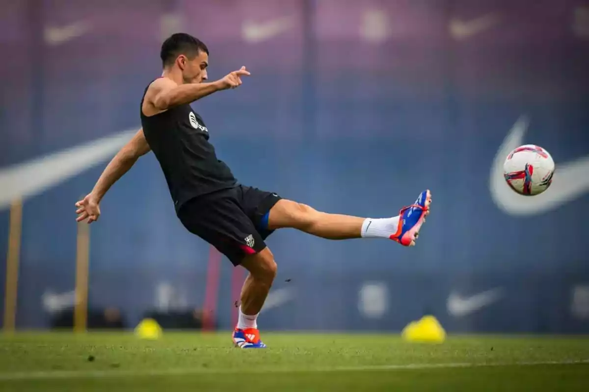 Un jugador de fútbol en un campo de entrenamiento pateando un balón con la pierna derecha extendida.