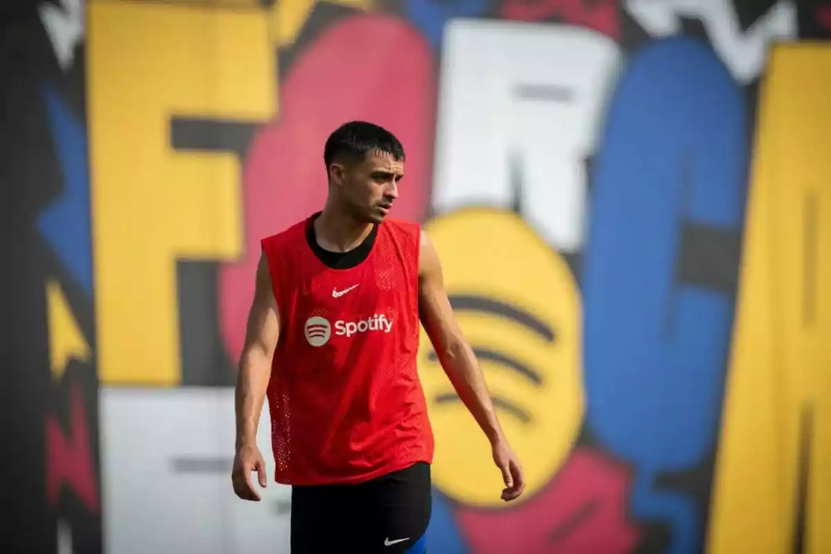 Jugador de fútbol con camiseta de entrenamiento roja de Spotify frente a un mural colorido.