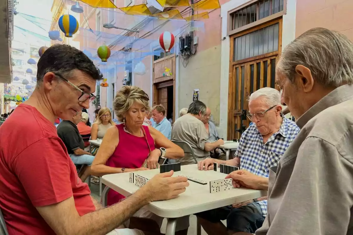 Un grup de persones juga al dòmino en una terrassa decorada amb globus de colors.