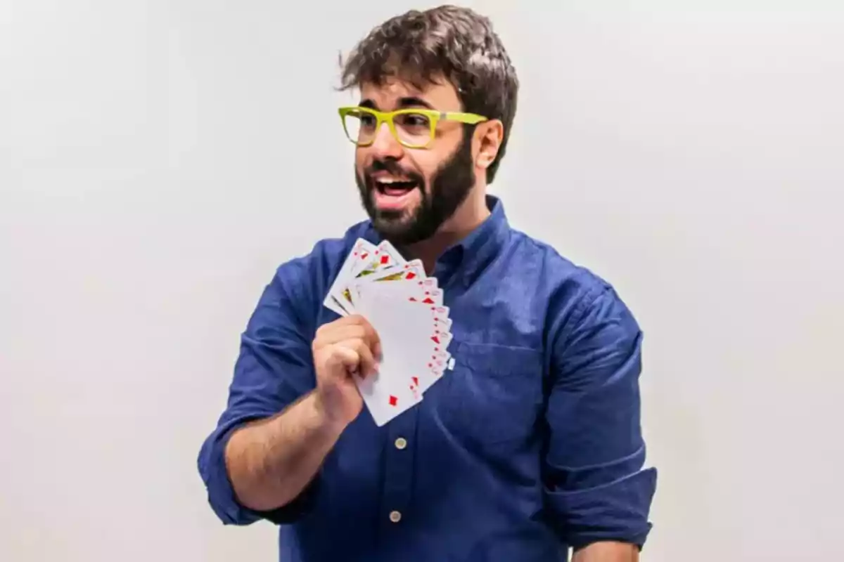 Home amb ulleres grogues i camisa blava mostrant un ventall de cartes mentre somriu Home amb ulleres grogues i camisa blava mostrant un ventall de cartes mentre somriu