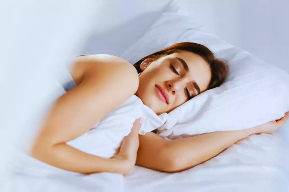 Mujer durmiendo plácidamente en una cama con sábanas blancas.