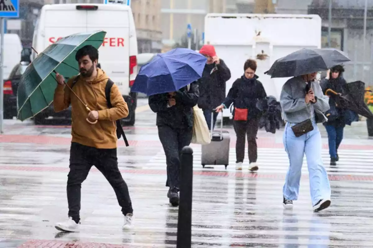 Diverses persones creuant un carrer amb paraigües en un dia de pluja a Santander Diverses persones creuant un carrer amb paraigües en un dia de pluja a Santander