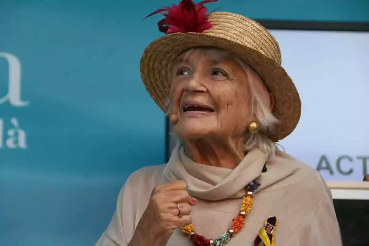 Una mujer mayor sonriente con sombrero de paja adornado con una flor roja y un collar colorido.