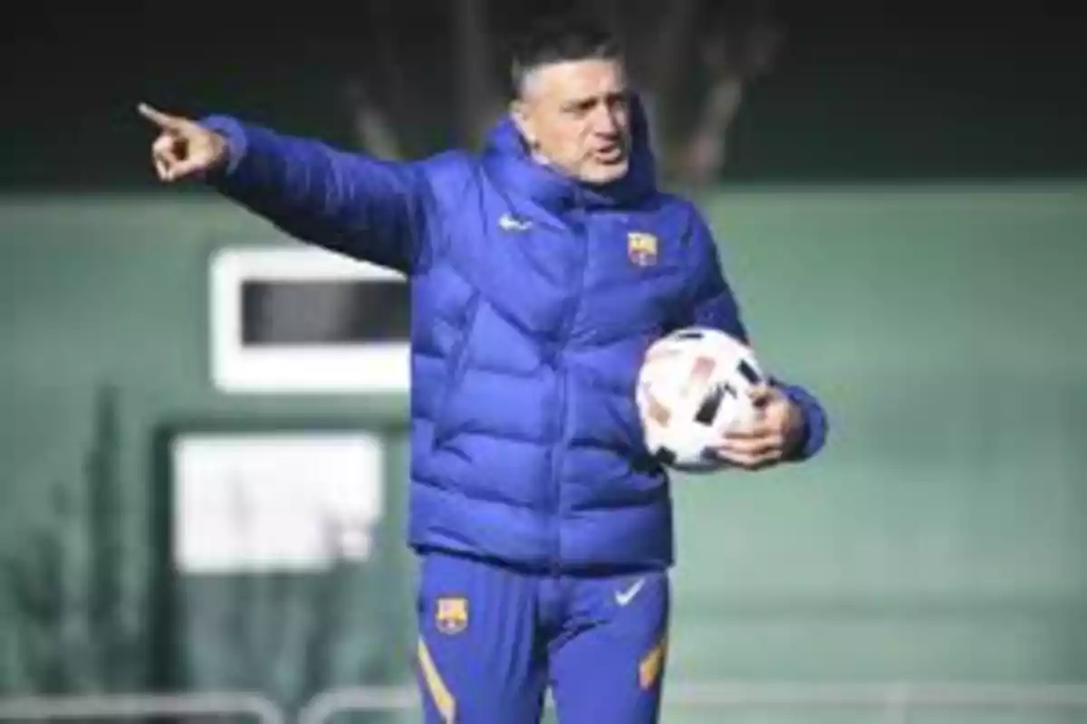 Entrenador de fútbol con chaqueta azul señalando mientras sostiene un balón.