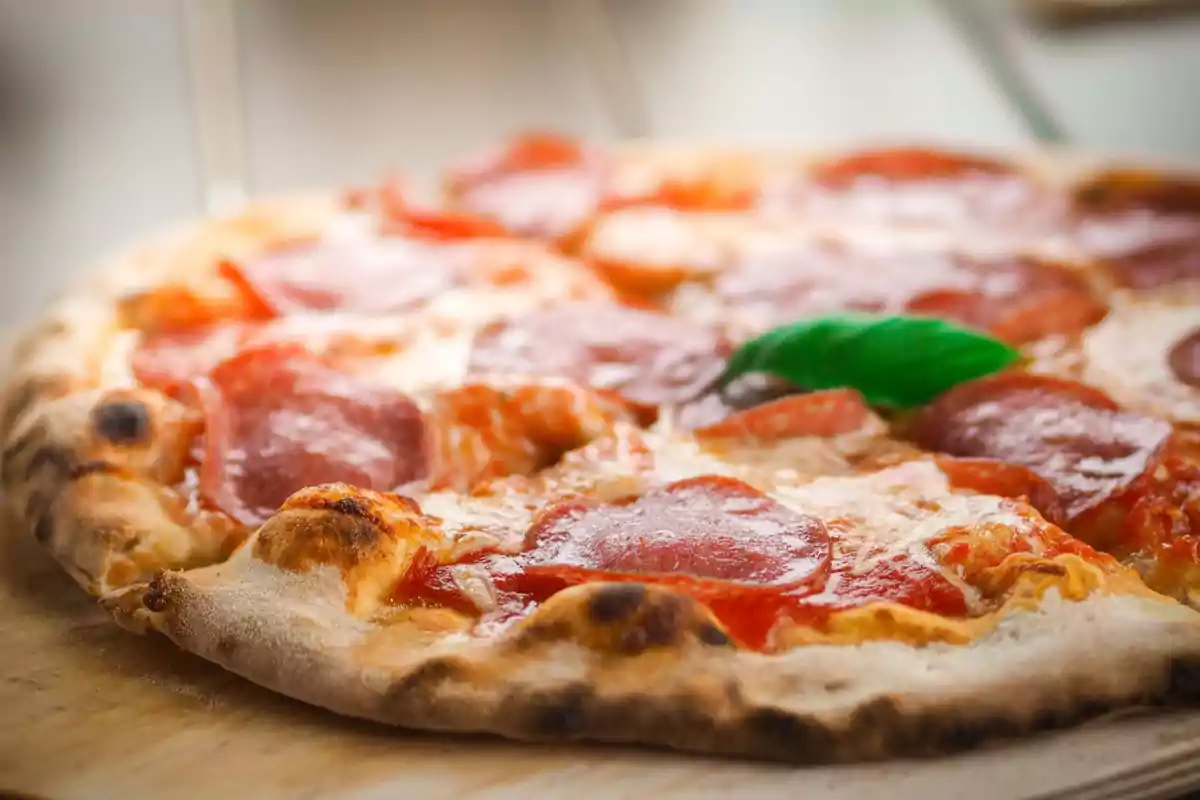 Una pizza de pepperoni con una hoja de albahaca sobre una tabla de madera. Una pizza de pepperoni con una hoja de albahaca sobre una tabla de madera.