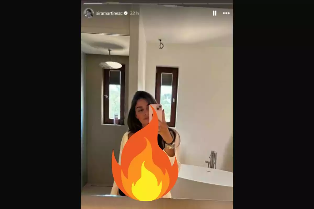 Una persona prenent una selfie davant d'un mirall en un bany, amb un emoji de foc cobrint part del seu cos.