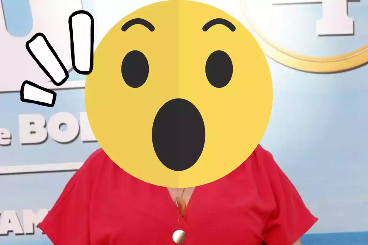 Persona con un emoji de sorpresa cubriendo su rostro, vistiendo una blusa roja y un collar, posando frente a un fondo con texto parcialmente visible.