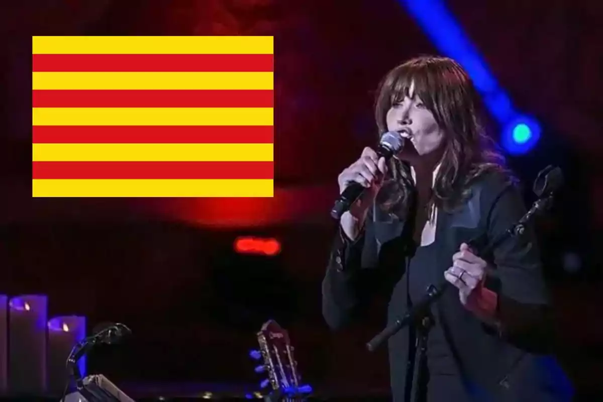 Una dona cantant en un escenari amb una bandera de Catalunya a la cantonada superior esquerra.