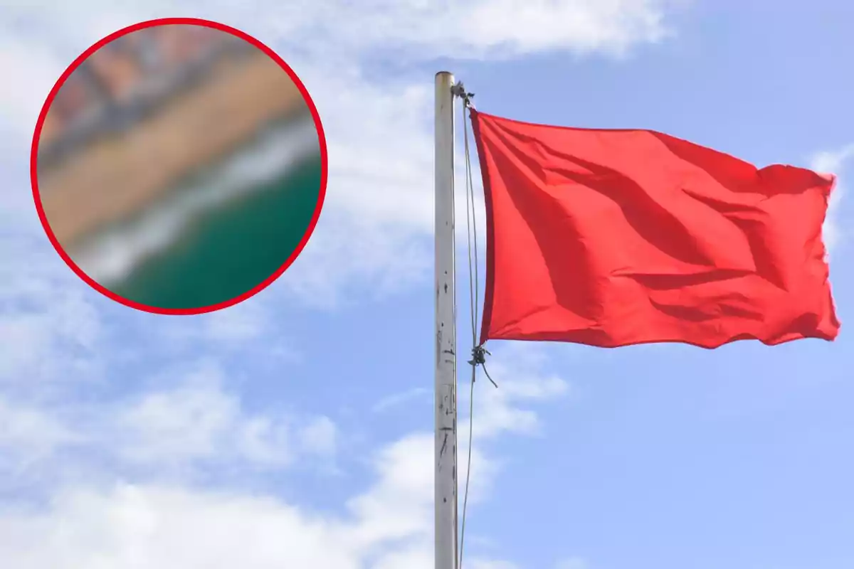 Una bandera roja ondea en un mástil con el cielo azul y nubes de fondo, y un círculo borroso en la esquina superior izquierda muestra una vista aérea de una playa.