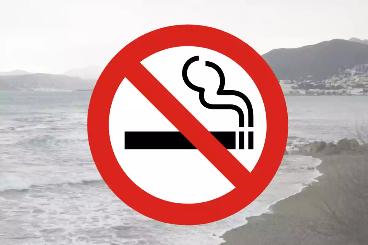 Símbol de prohibit fumar sobre una platja amb muntanyes al fons