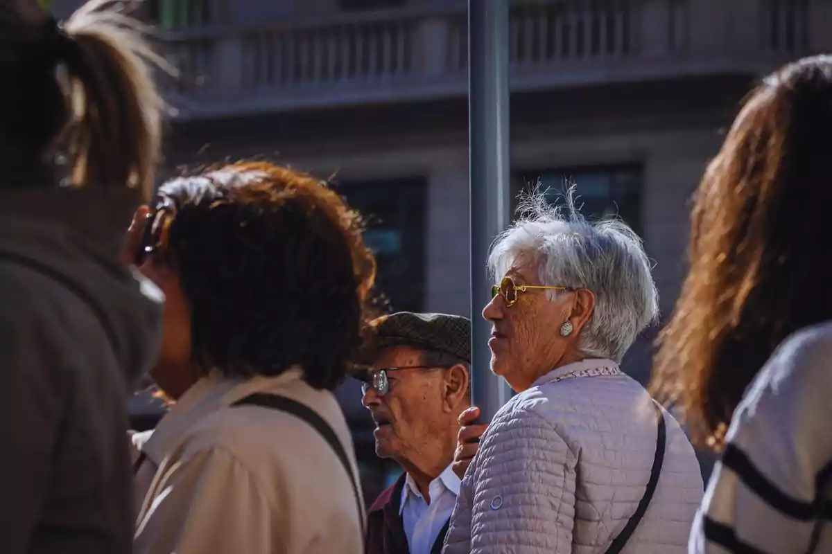 Un grupo de personas de diferentes edades camina por una calle soleada en una ciudad.