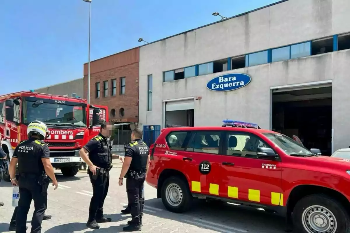 Diversos policies i bombers estan reunits davant d'una nau industrial amb vehicles d'emergència estacionats al carrer.
