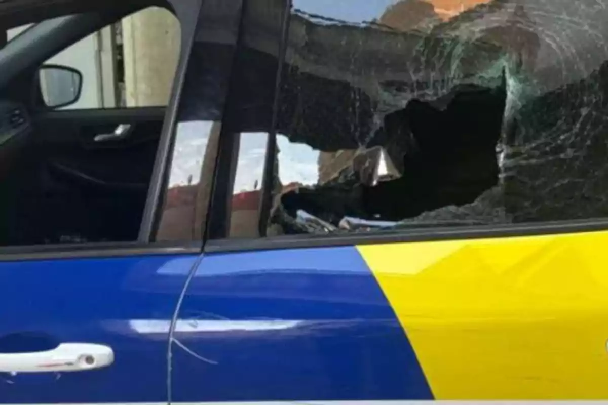 Un cotxe amb la finestra trencada i la porta pintada de blau i groc.