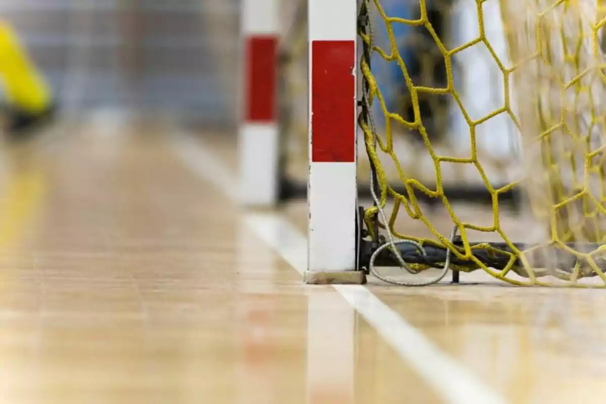 Primer pla d'un pal de porteria de futbol sala amb una xarxa groga en un terra de fusta.