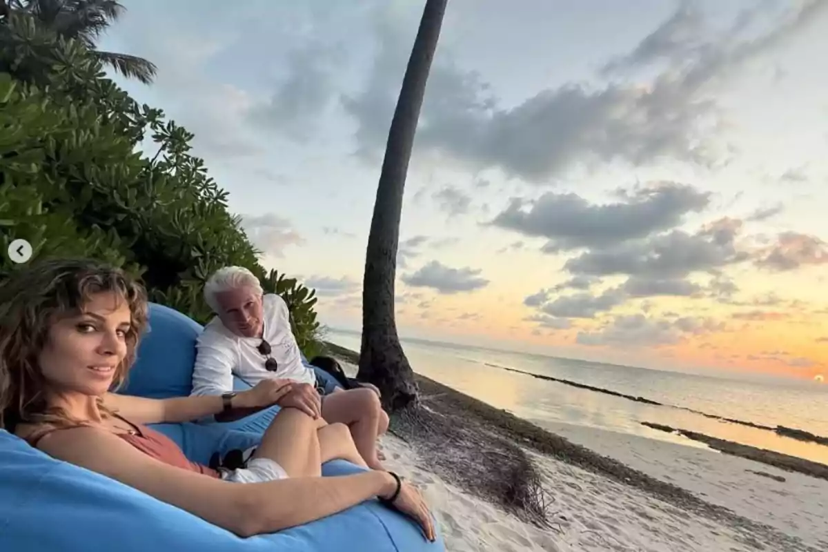 Alejandra Silva and Richard Gere relaxing on a beach at sunset, sitting in blue chairs with the sea and cloudy sky in the background. Alejandra Silva and Richard Gere relaxing on a beach at sunset, sitting in blue chairs with the sea and cloudy sky in the background.
