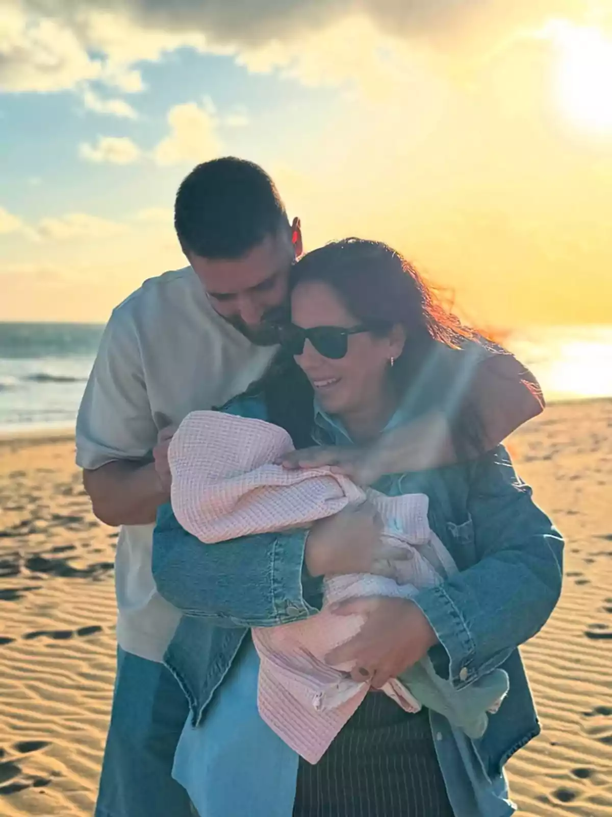David Rodríguez y Anabel Pantoja sonriente sostiene a Alma envuelto en una manta en la playa al atardecer. David Rodríguez y Anabel Pantoja sonriente sostiene a Alma envuelto en una manta en la playa al atardecer.