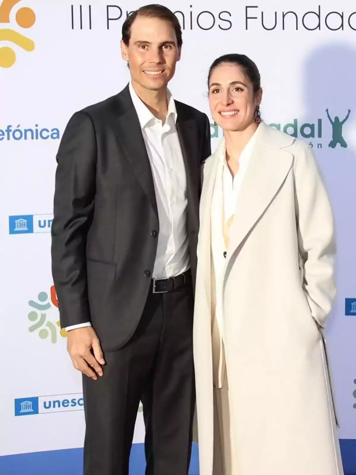 Rafa Nadal i Xisca Perelló posen juntes en un esdeveniment formal amb un fons que mostra logotips d'organitzacions. Rafa Nadal i Xisca Perelló posen juntes en un esdeveniment formal amb un fons que mostra logotips d'organitzacions.