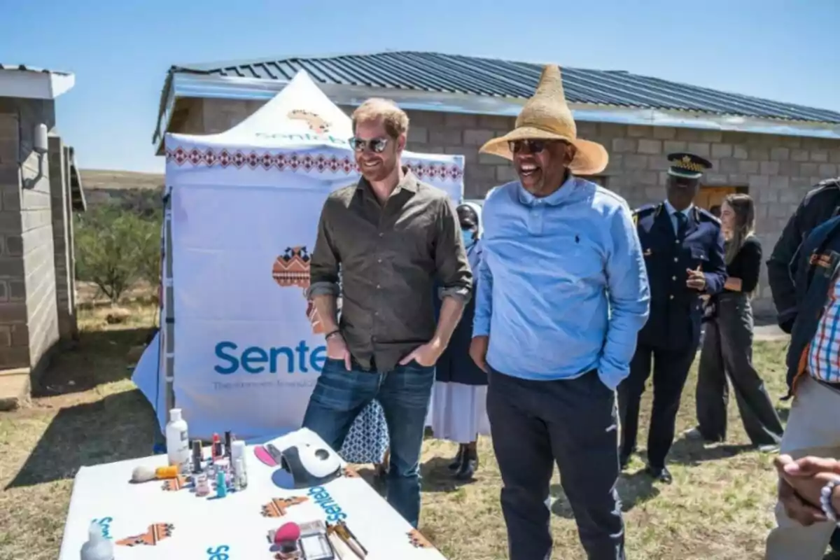 Els prínceps Harry i Seeiso somriuen mentre observen una taula amb productes en un esdeveniment a l'aire lliure, un d'ells porta un barret tradicional i hi ha una carpa de fons. Els prínceps Harry i Seeiso somriuen mentre observen una taula amb productes en un esdeveniment a l'aire lliure, un d'ells porta un barret tradicional i hi ha una carpa de fons.