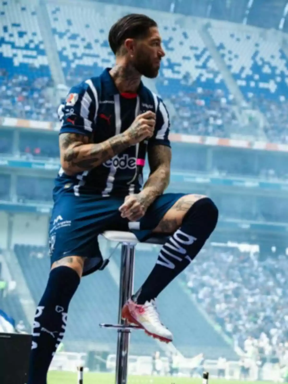 Sergio Ramos amb uniforme blau i blanc assegut en un tamboret en un estadi. Sergio Ramos amb uniforme blau i blanc assegut en un tamboret en un estadi.