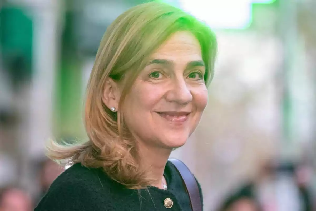 La infanta Cristina sonriente con cabello rubio y suelto, usando un abrigo oscuro, en un entorno urbano desenfocado. La infanta Cristina sonriente con cabello rubio y suelto, usando un abrigo oscuro, en un entorno urbano desenfocado.