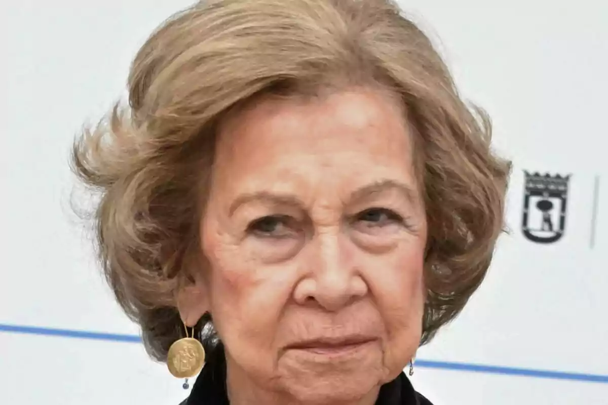 Una persona gran amb cabell curt i canós -que és la reina Sofia- porta arracades daurades i està en un entorn exterior.