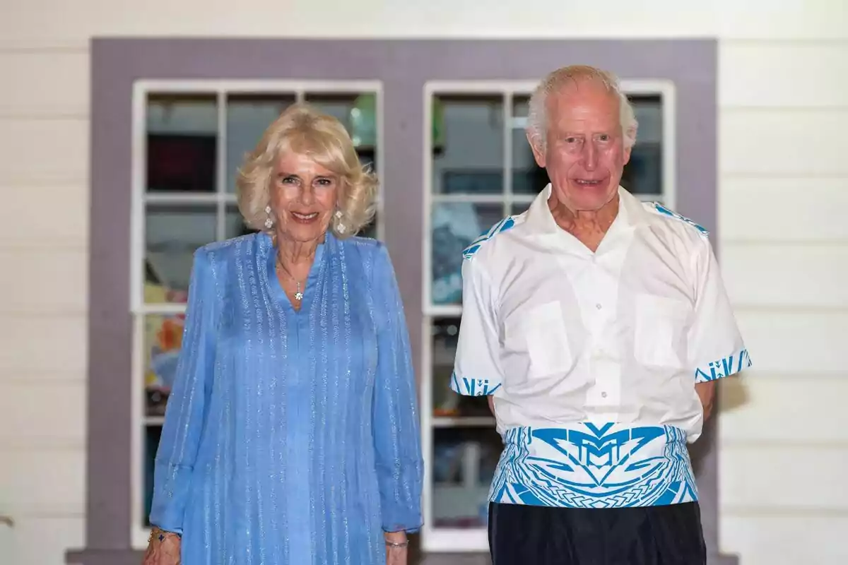 La reina Camila i Carles III posen junts davant d'una finestra, una dona porta un vestit blau i un home porta una camisa blanca amb detalls blaus. La reina Camila i Carles III posen junts davant d'una finestra, una dona porta un vestit blau i un home porta una camisa blanca amb detalls blaus.