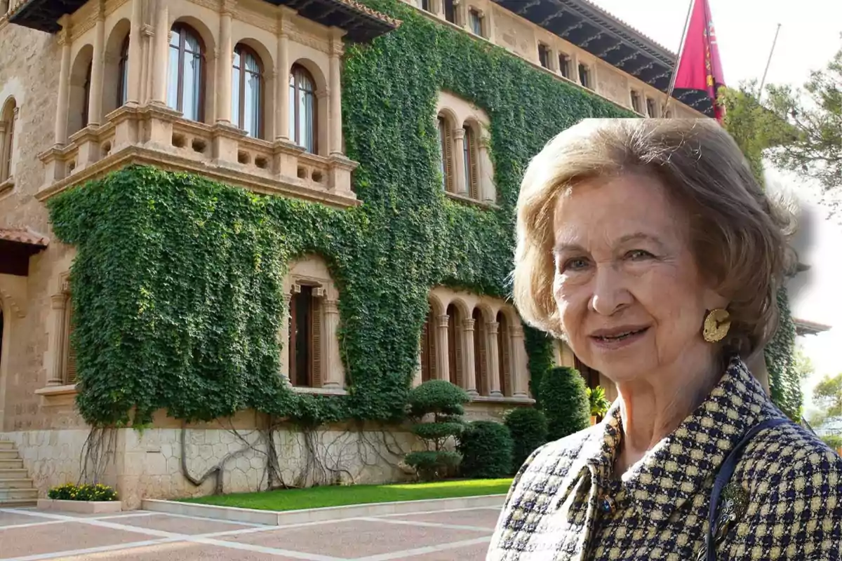 Una mujer mayor sonriente con un edificio histórico cubierto de hiedra en el fondo.