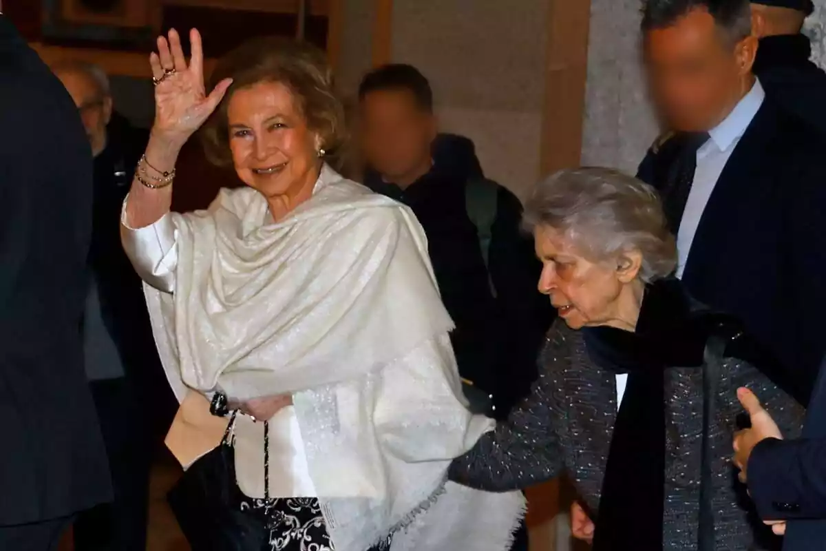 La reina Sofia somrient i saludant amb un mocador blanc al cos i Irene de Grècia agafant-s'hi La reina Sofia somrient i saludant amb un mocador blanc al cos i Irene de Grècia agafant-s'hi