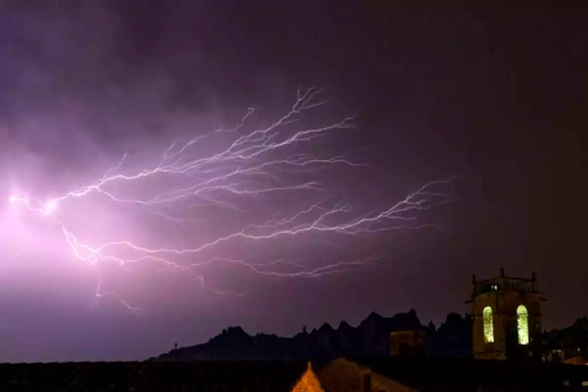 Raig il·luminant el cel nocturn sobre un paisatge urbà amb una torre il·luminada.