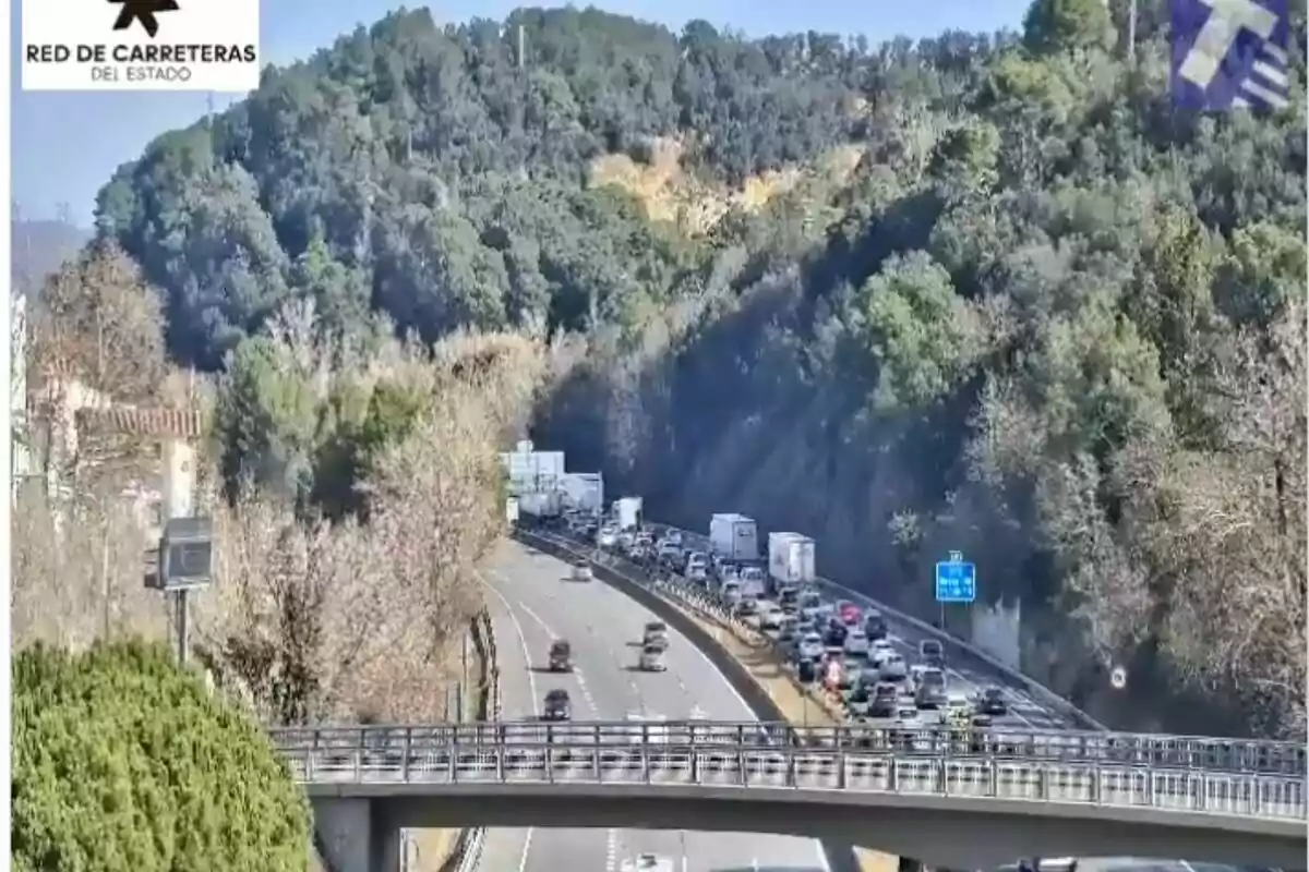 Una carretera amb trànsit dens envoltada d'arbres i turons sota un cel clar.