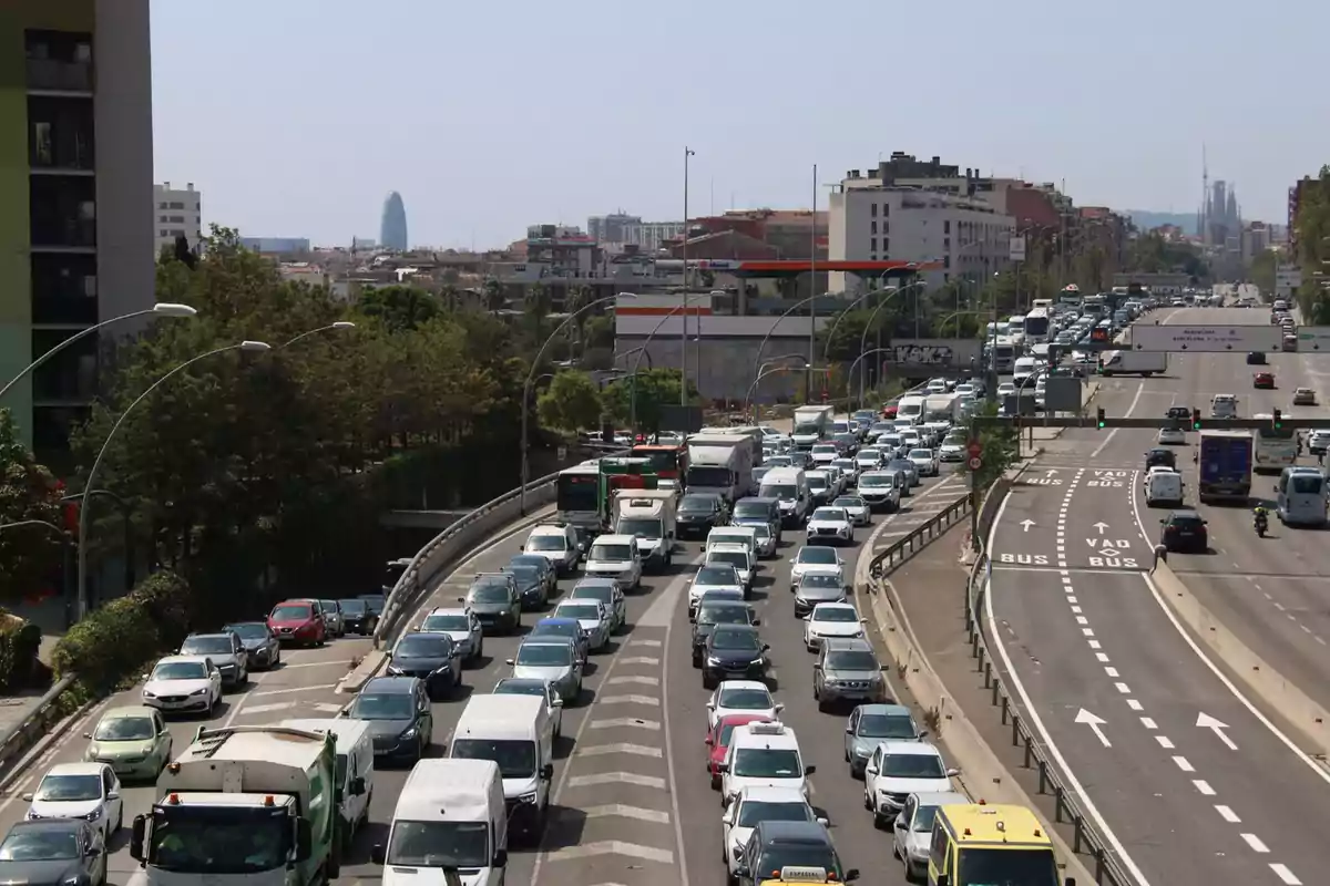 Trànsit dens en una autopista urbana amb múltiples carrils i edificis al fons.