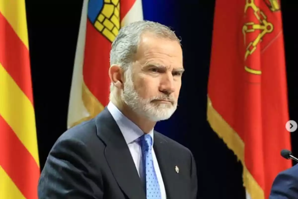Un home amb barba i vestit fosc està davant de diverses banderes acolorides. Un home amb barba i vestit fosc està davant de diverses banderes acolorides.